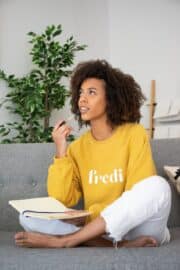 Woman sitting on a couch with pen and notebook thinking